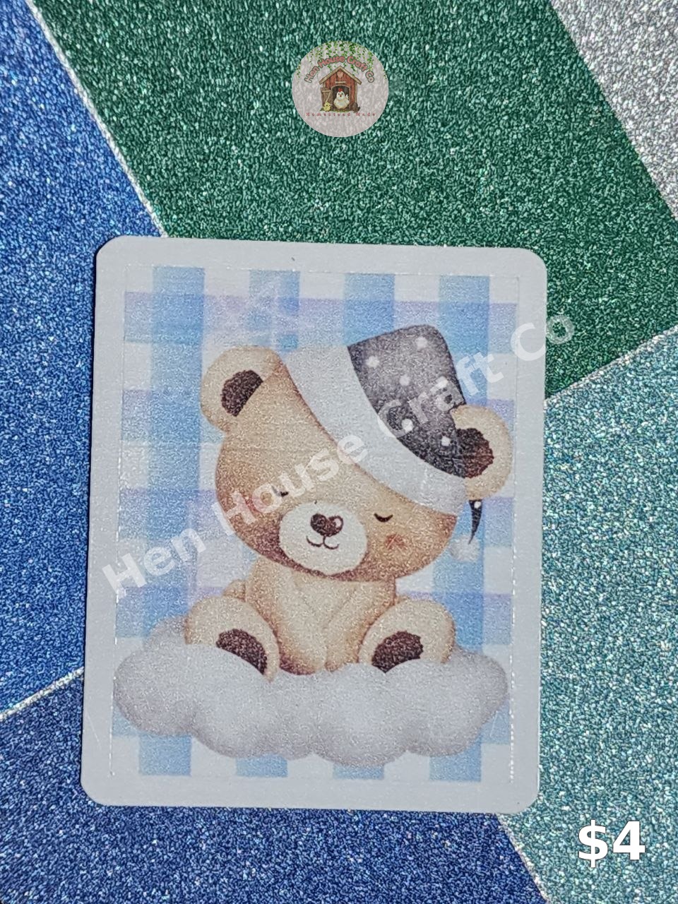 Blue Plaid Dreamy Bear sticker — a sleeping teddy bear in a starry nightcap resting on a cloud, on a soft blue plaid background
