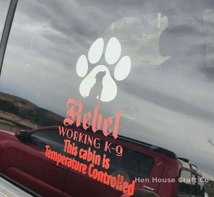 Custom cut-vinyl decal on a truck window: a white paw print with a sitting dog silhouette inside, above the name Rebel in coral script, then WORKING K-9 and This cabin is Temperature Controlled.
